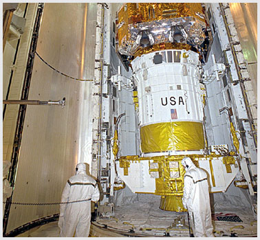 Image of workers in the Payload Changeout Room with a satellite in the shuttle bay.