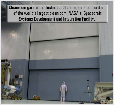 Worker in a bunny suit standing by the entrance door to the Spacecraft Systems Development and Intregration facility - the world's largest cleanroom.