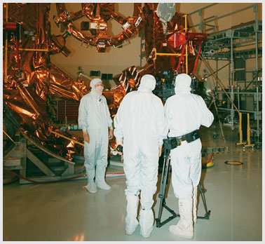 Photo of workers in bunny suits working on a satellite.